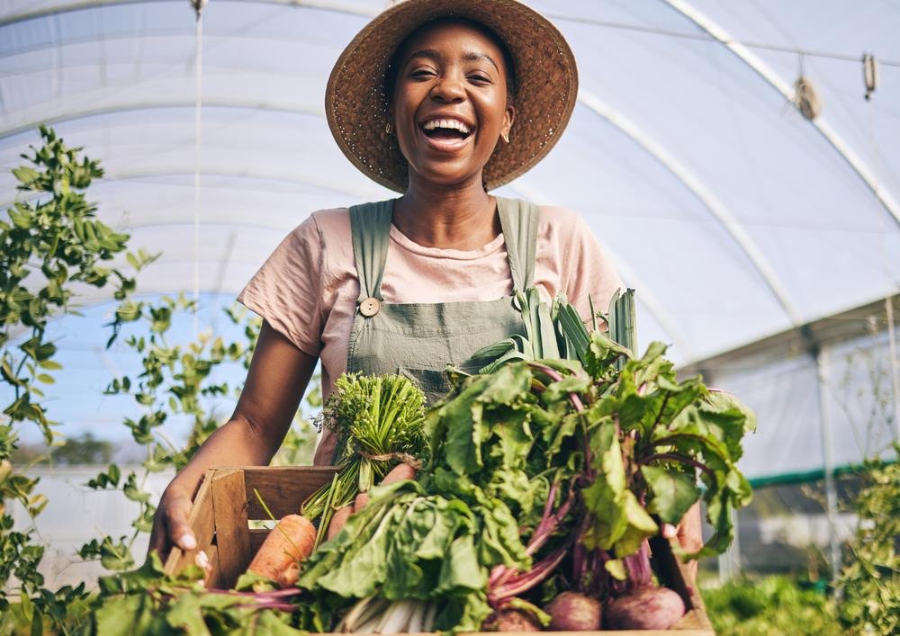 A smiling woman holding freshly harvested greens in a greenhouse