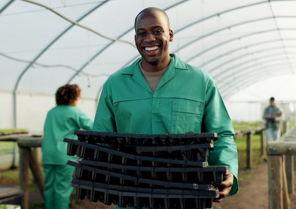 A farmer carrying seedling trays in a greenhouse